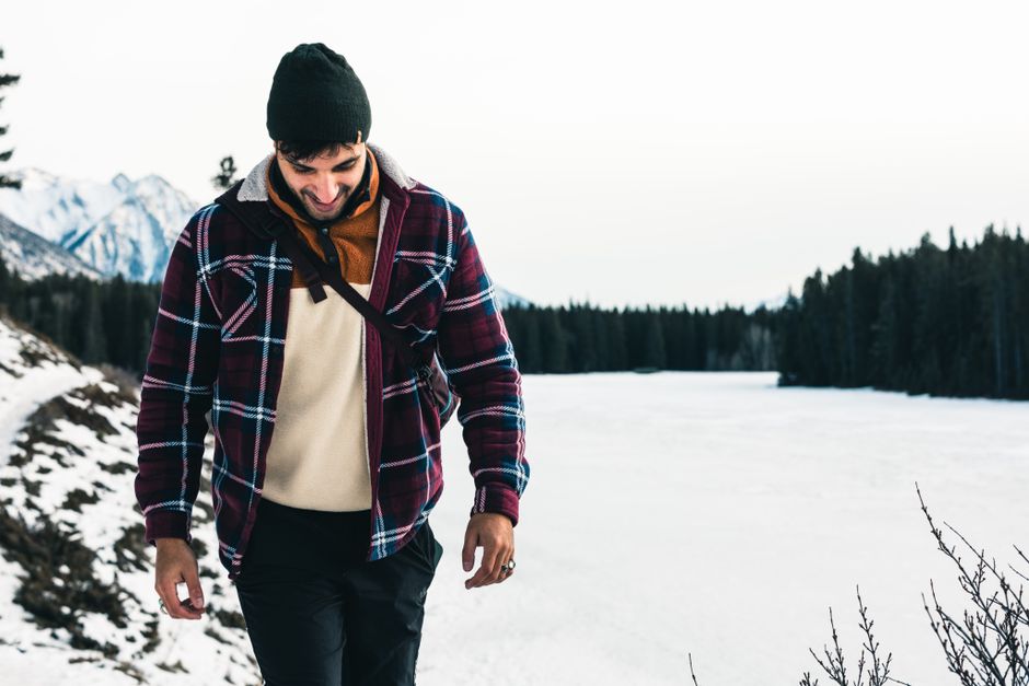 A man enjoys winter hiking in Banff, Canada, surrounded by snowy mountains and a frozen la
