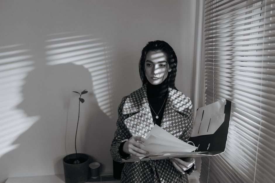 Business woman in black and white, reviewing documents with blinds creating shadows.