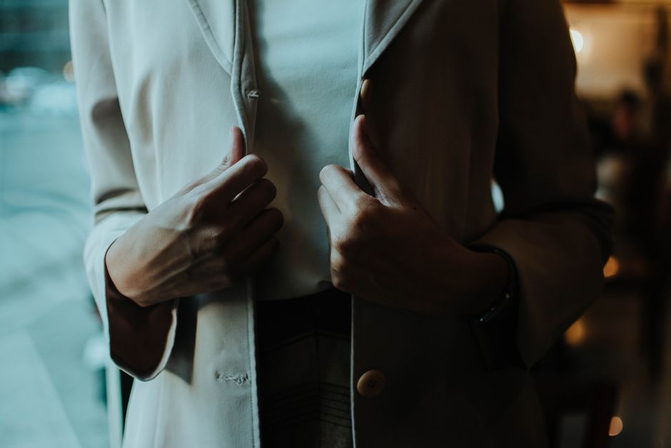 Close-up of a woman adjusting her blazer, showcasing elegance and style indoors.