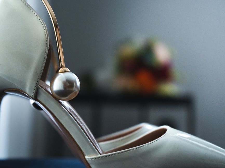 Close-up of a stylish white high heel shoe featuring a pearl embellishment, perfect for formal occasions.