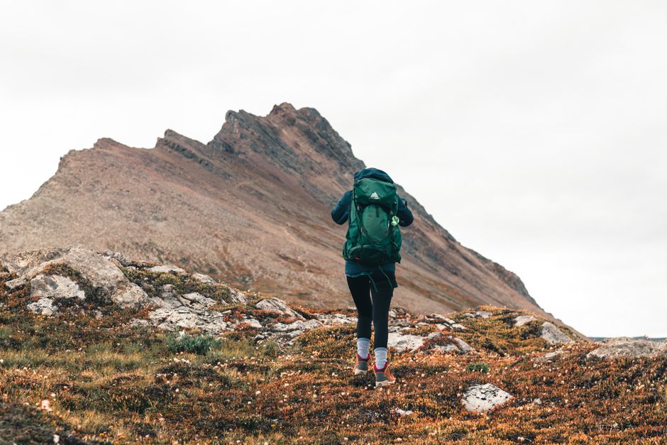 A lone hiker with a backpack walks through a rugged mountainous terrain.