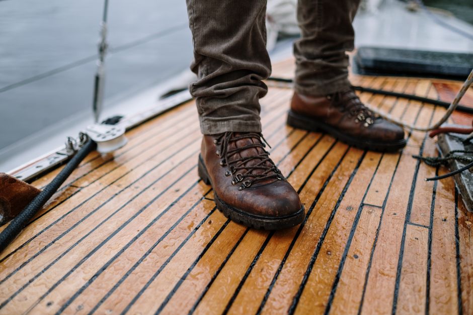 Close-up of rugged leather hiking boots standing on a wet wooden boat deck with ropes in view.