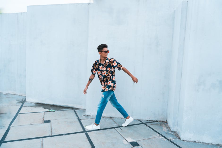 A fashionable man walks outdoors in a stylish floral shirt and jeans, exuding a confident vibe.