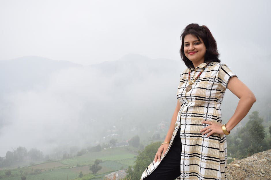 A woman smiling confidently on a misty mountain, surrounded by lush greenery and foggy hills.