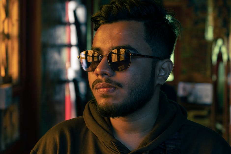 Moody portrait of a man wearing sunglasses indoors at night, illuminated by warm lighting.