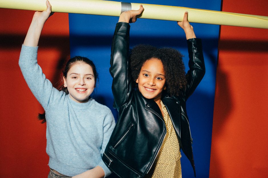 Two happy girls hanging from a bar with colorful background. Bright and playful indoors fun.