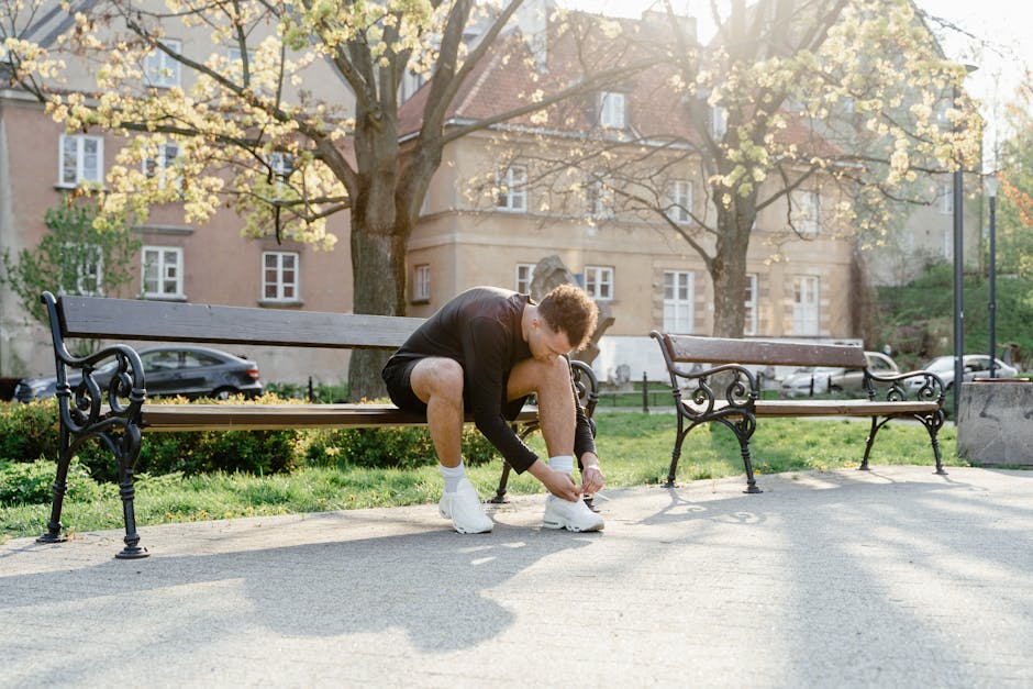 Adult man tying shoes on park bench in morning sunlight, ready for jogging.
