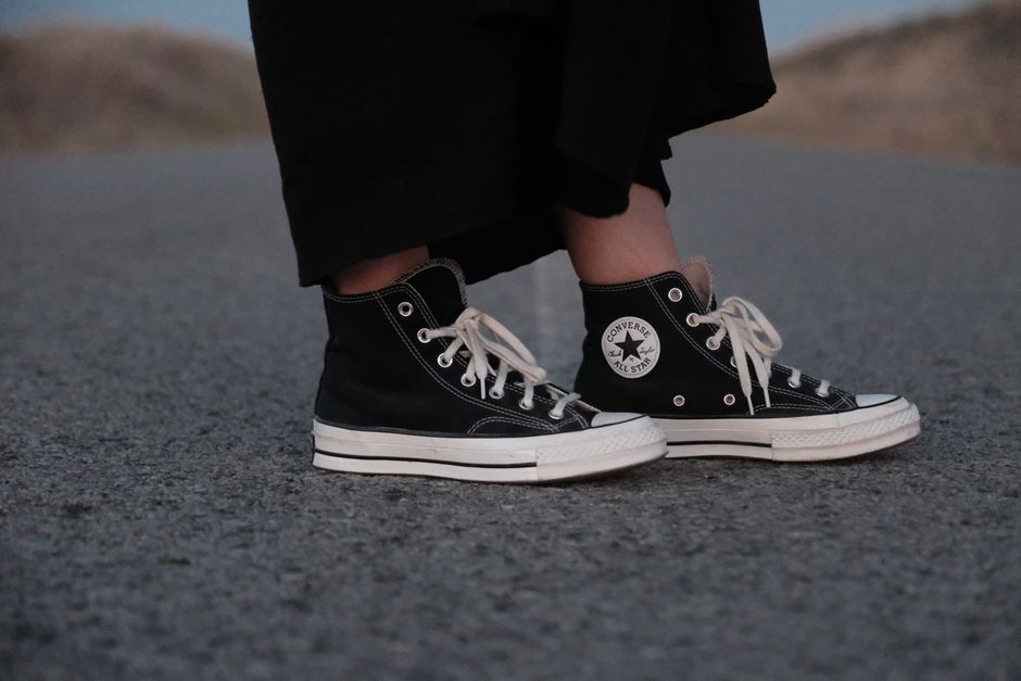 Close-up of a woman wearing black Converse sneakers on a road, showcasing casual outdoor street style.