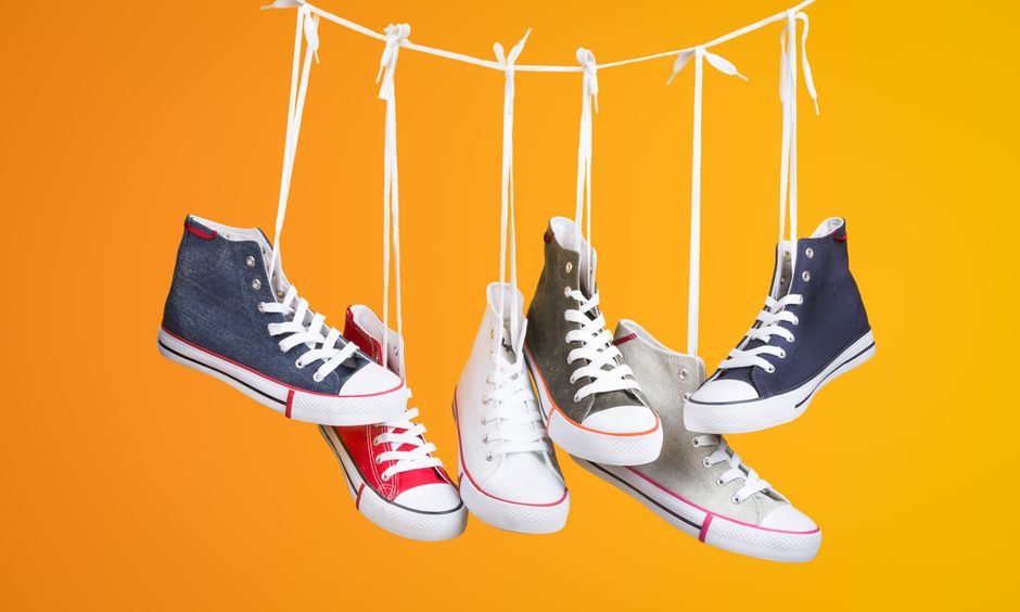 Stylish sneakers in various colors hanging with laces on a vivid orange backdrop. Ideal for fashion themes.