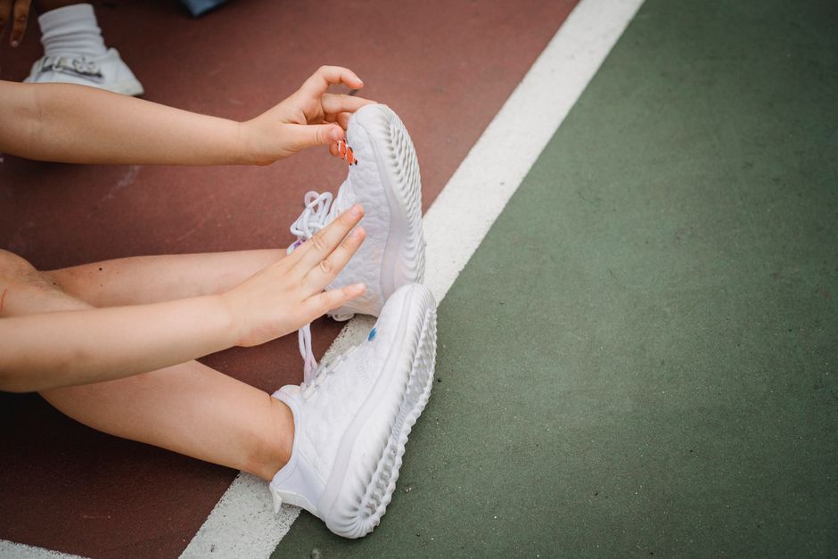 A child adjusting white sneakers while sitting on a colored sports court.
