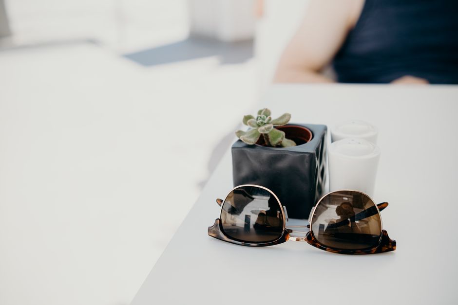 Elegant sunglasses and potted plant on a white table, perfect for summer cafe settings.