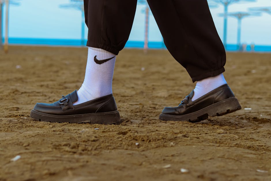 Fashionable loafers and white socks on a sandy beach, representing casual summer style.