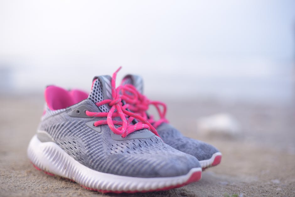 A pair of modern grey and pink sneakers resting on a sandy beach, ideal for footwear and lifestyle themes.