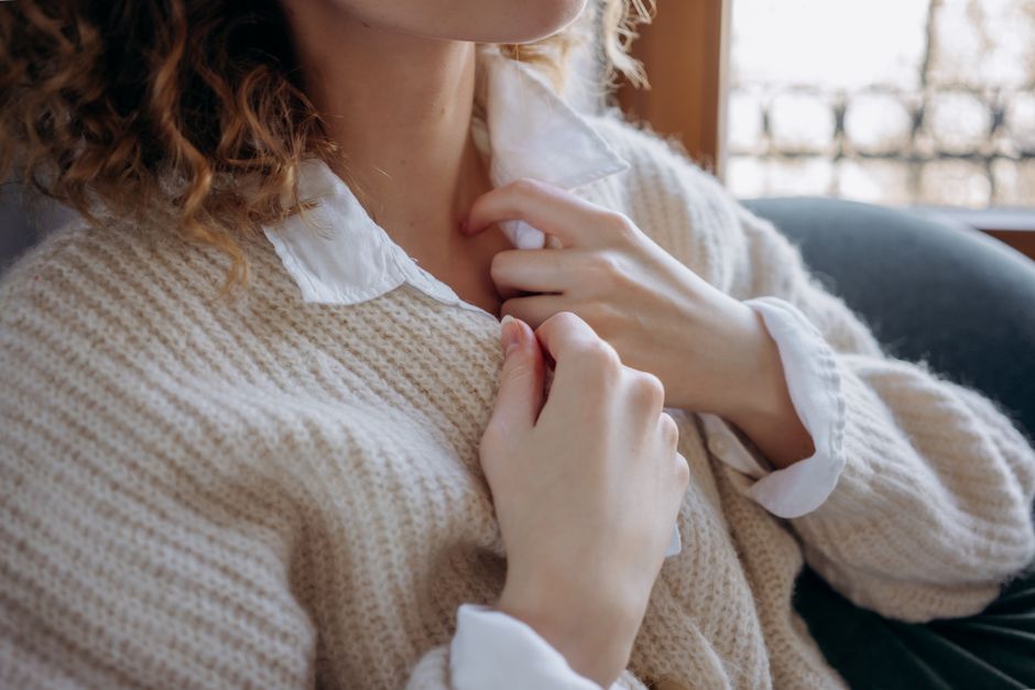 Close-up of hands pulling a soft knitted sweater collar indoors, capturing warmth and comfort.
