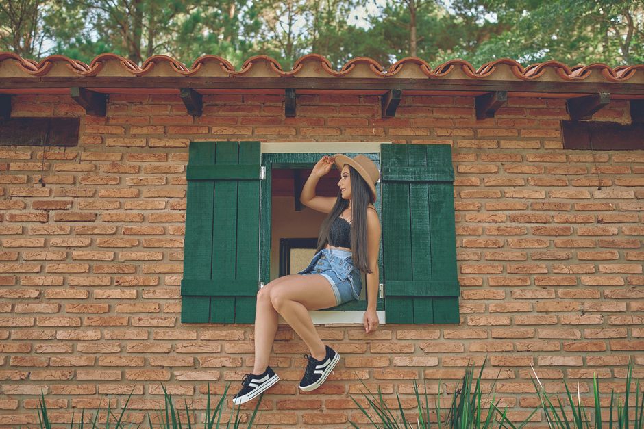 Woman in summer attire sitting on a rustic brick building's window ledge.