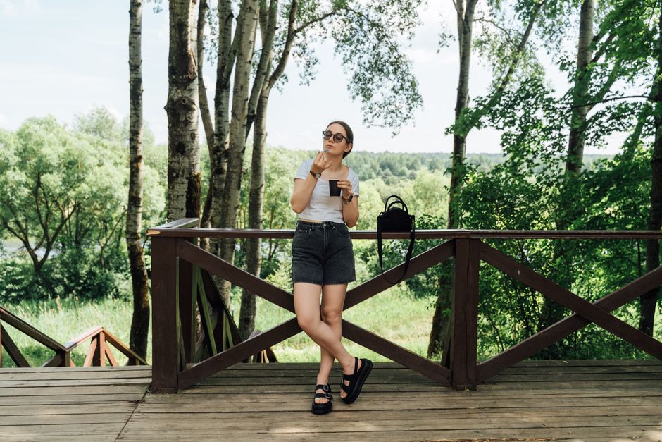A woman enjoying a drink while relaxing on a wooden terrace surrounded by lush summer forest.