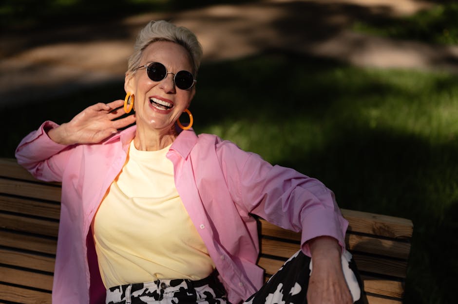 Chic elderly woman laughing and relaxing on a park bench under the sun.
