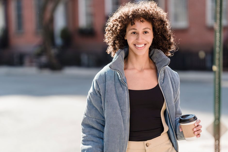 Confident young ethnic female millennial with curly dark hair in trendy outfit smiling and