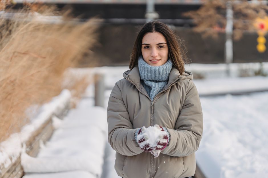 Content young female wearing warm clothes and mittens in warm clothes holding snow in hand