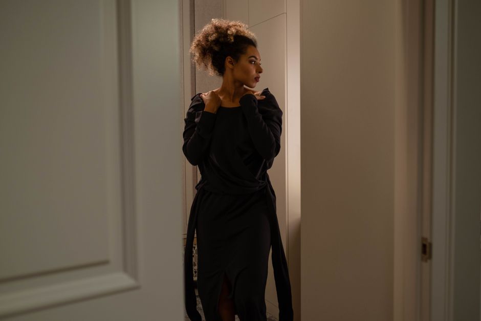 Stylish woman in a black dress adjusting her hair indoors, exuding elegance and poise.