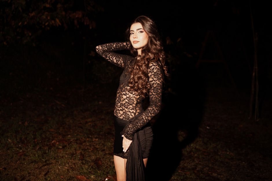 Elegant woman poses in a lace dress outdoors at night, exuding confidence and style.