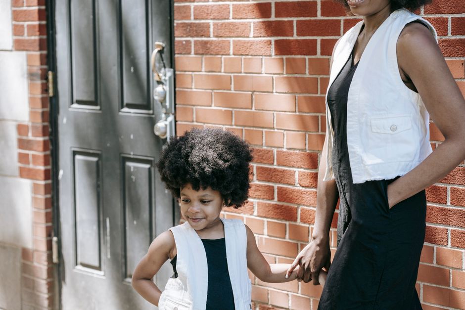 A mother and daughter with matching outfits and afro hair holding hands outdoors.