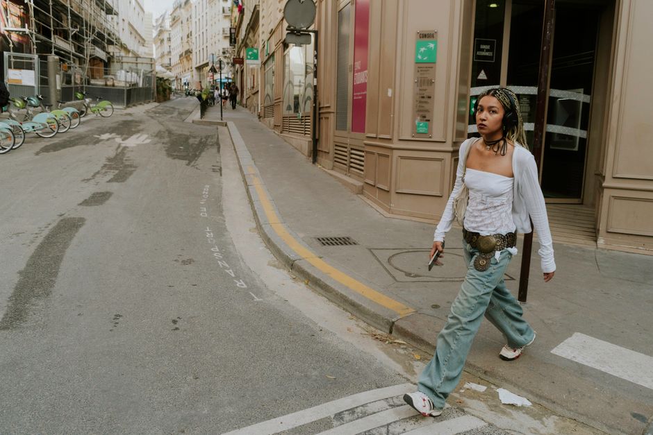 A young woman walks confidently across a city street, showcasing urban style fashion.