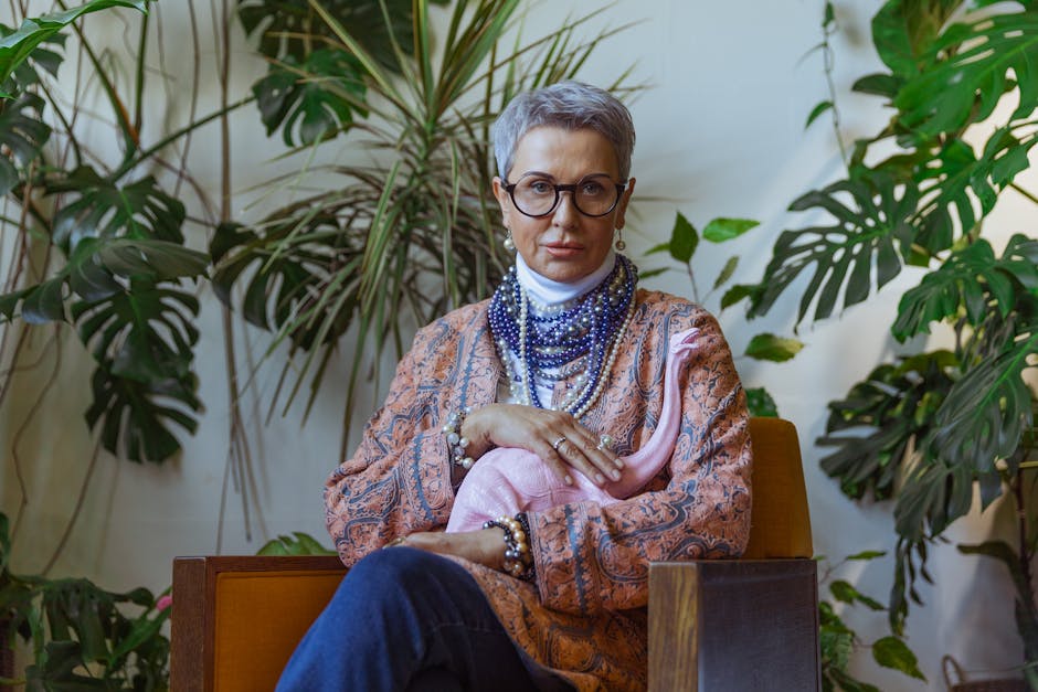 Stylish senior woman with eyeglasses and boho fashion sitting amidst lush greenery.