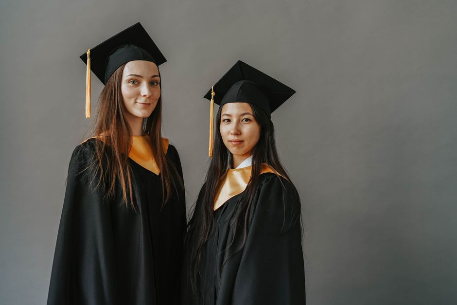 Two graduates posing in traditional gowns and caps celebrating their academic achievements.
