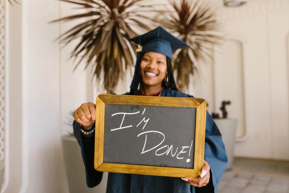 A proud graduate holds a mini blackboard with 'I'm Done!' indoors, celebrating academic success.