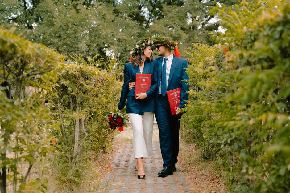 Happy couple celebrating graduation outdoors in Italy, wearing laurel wreaths.