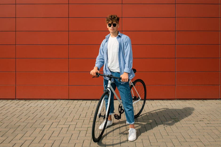Stylish young man standing with a bicycle against a modern red wall in a city setting.