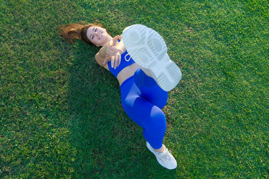 Woman lying on grass, stretching in blue sportswear, enjoying outdoor exercise.