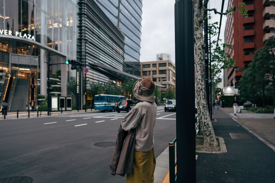 A person stands at a Tokyo street corner near modern buildings, capturing urban life.