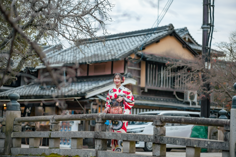 Asian woman in a kimono standing on a traditional bridge in a Japanese village.