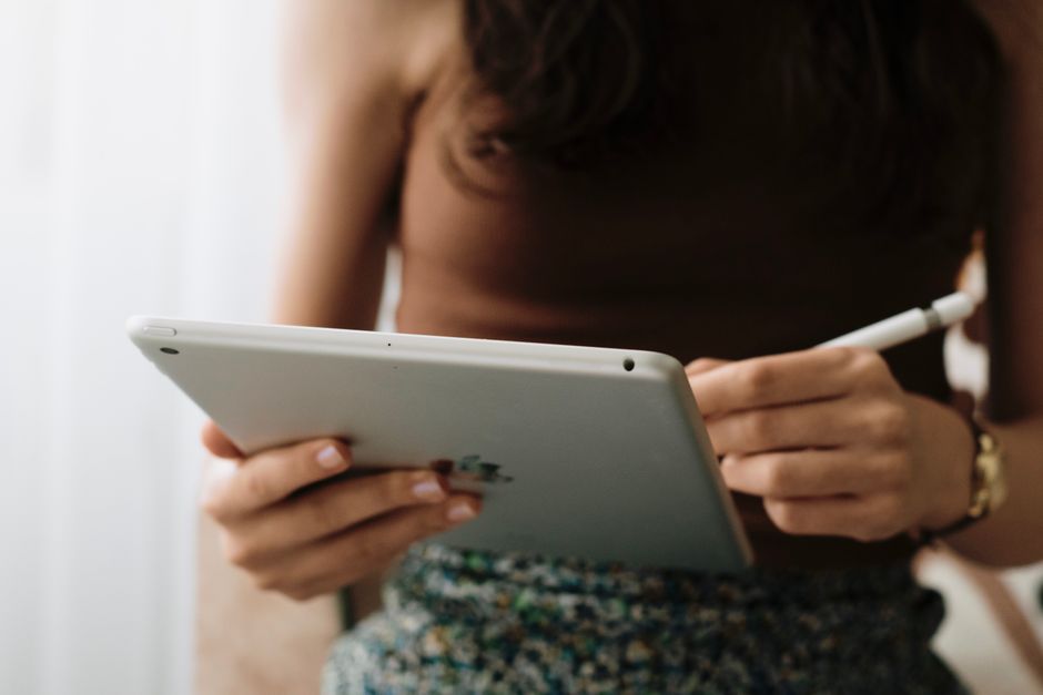 A woman using a tablet with a stylus indoors, symbolizing relaxation and modern technology.