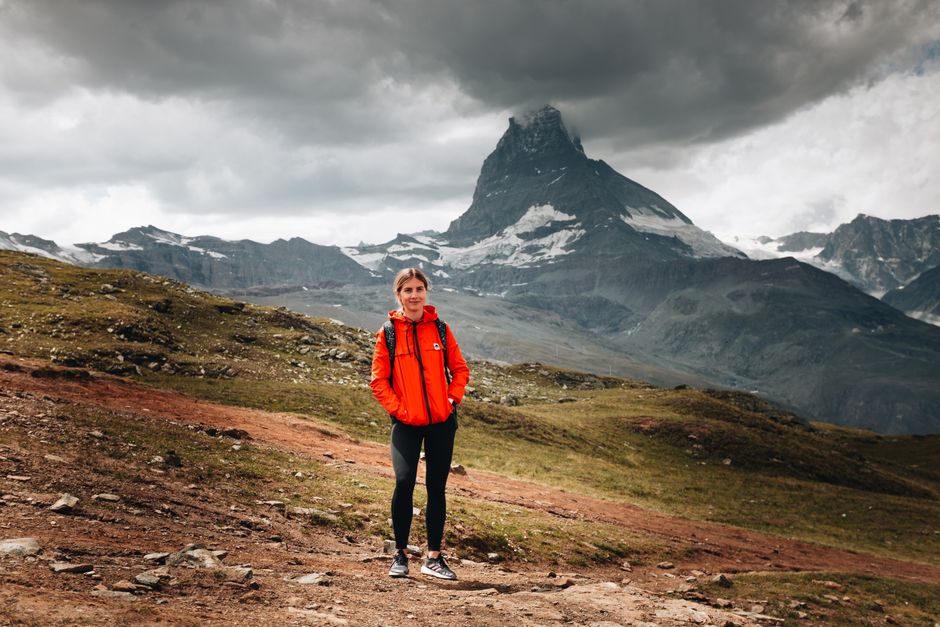 A woman in a red jacket stands before the dramatic Matterhorn mountain, showcasing the beauty of nature and adventure.