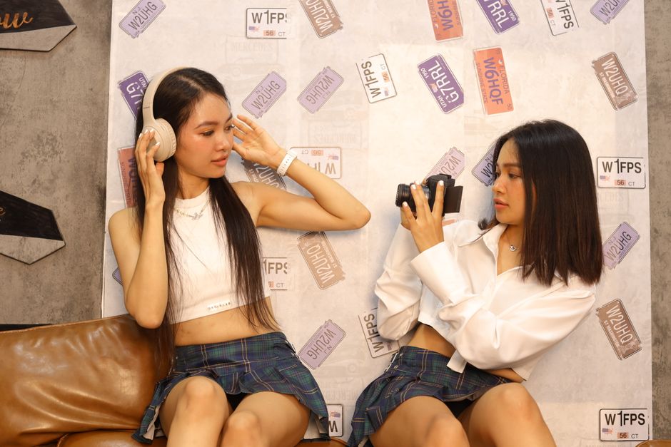 Two young women indoors, one with headphones, the other with a camera, enjoying a creative moment.