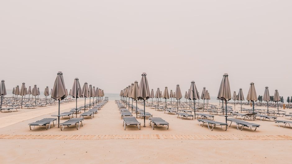 Serene view of empty beach in Rethymno, Greece with aligned sunbeds and umbrellas.