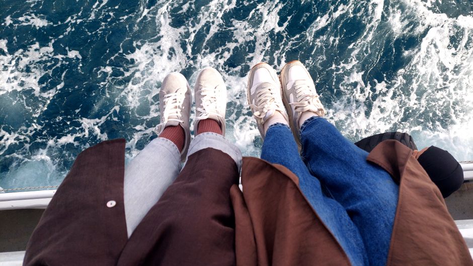Two people with white sneakers overlooking the ocean, enjoying a seaside adventure.