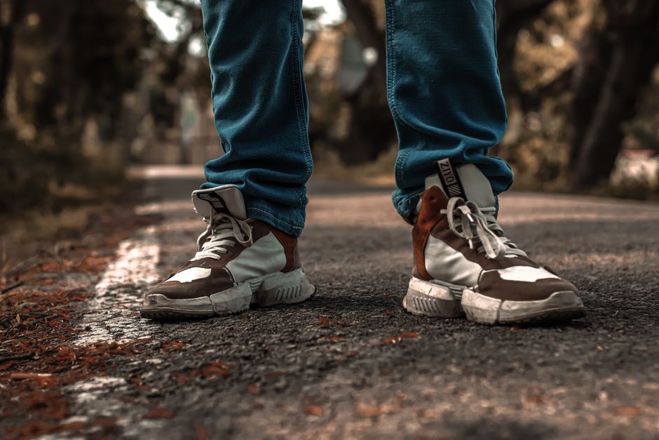 Detailed close-up of worn sneakers on a concrete pavement with denim jeans in an outdoor setting.
