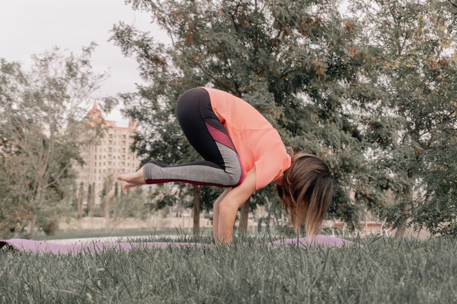A woman holds a yoga pose on a mat in a park, showcasing balance and focus.