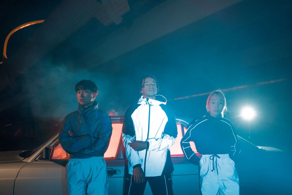 Group of three individuals standing by a car under night lights.