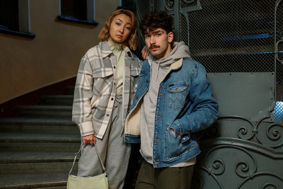 A fashionable couple poses on a staircase, showcasing modern streetwear style.