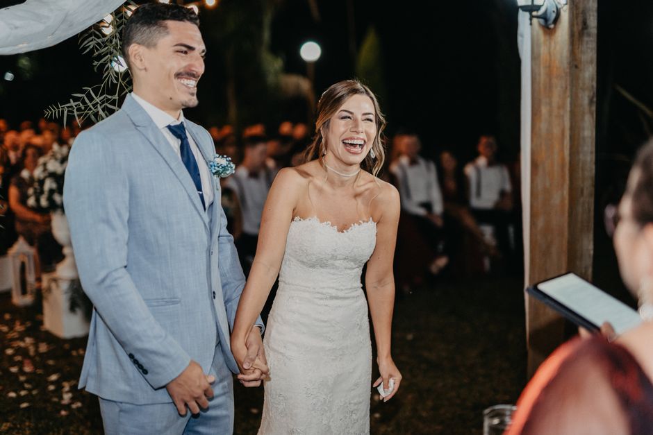 Bride and groom laughing and holding hands during a nighttime outdoor wedding ceremony.