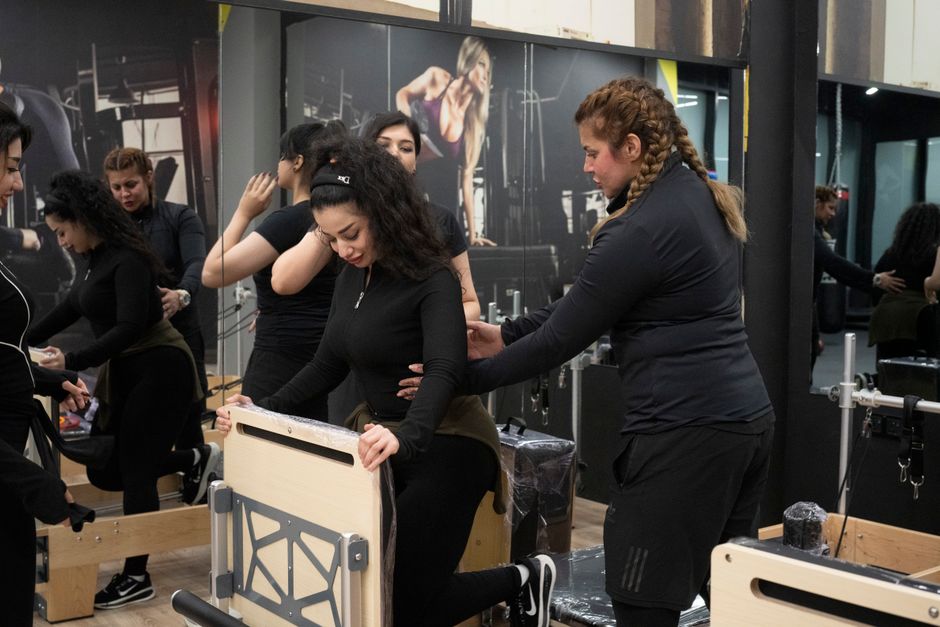 Women participating in a Pilates class with guidance from an instructor in a gym setting.