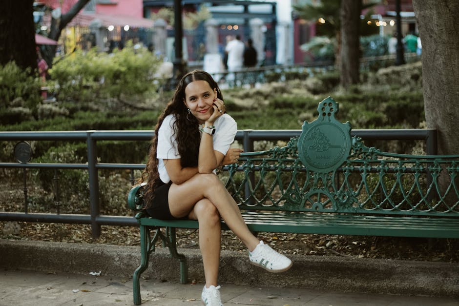 A young woman sitting on a decorative park bench embracing a relaxed moment outdoors.