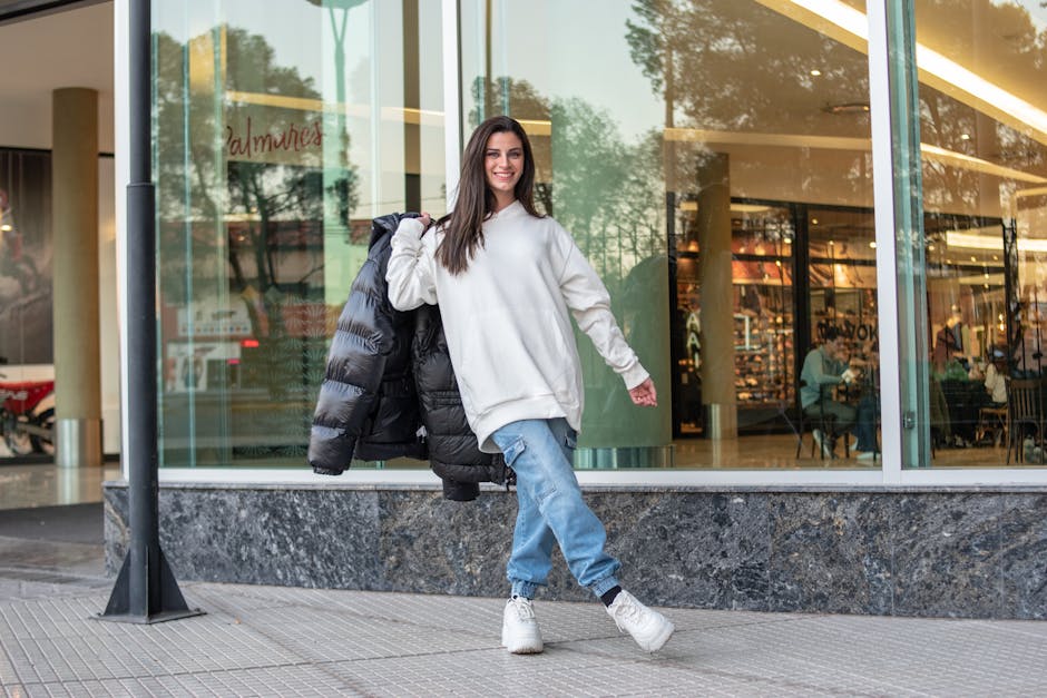Smiling woman in casual street fashion standing outside a modern shopping complex.