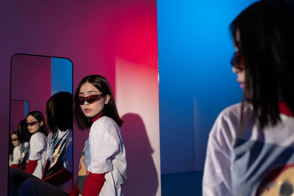 Fashionable woman in reflective mirror setting with vibrant red and blue lighting.