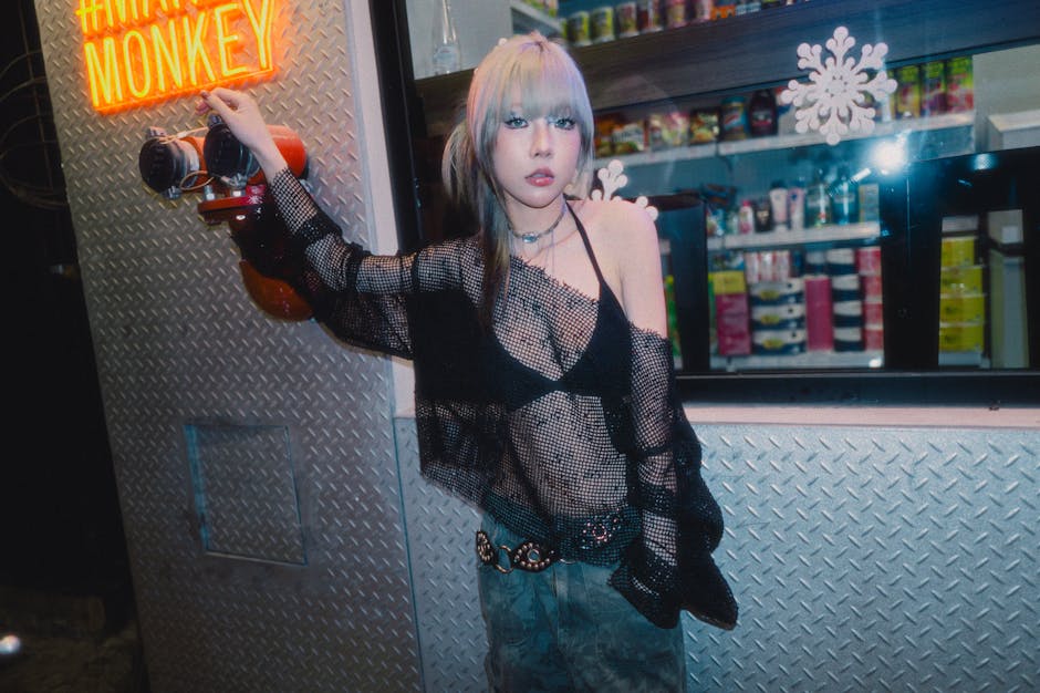 Young woman in edgy fashion poses by neon sign in urban setting, exuding confidence.